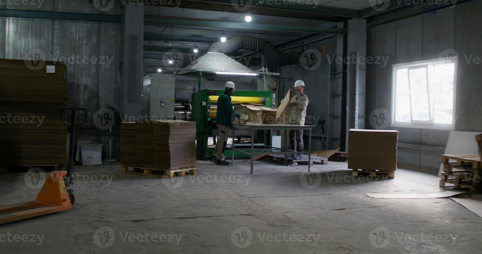Two men work in a cardboard factory. They take the cardboard cut by the machine photo