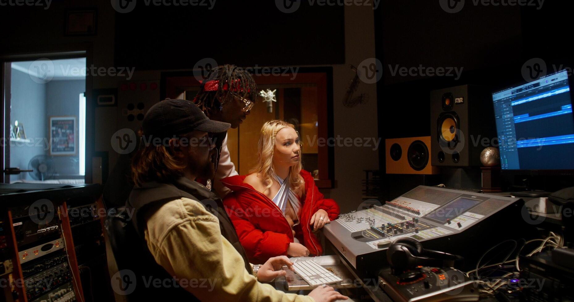 The sound engineer talks to the musicians after recording the song in the studio. They are sitting in front of the equipment in the control room photo