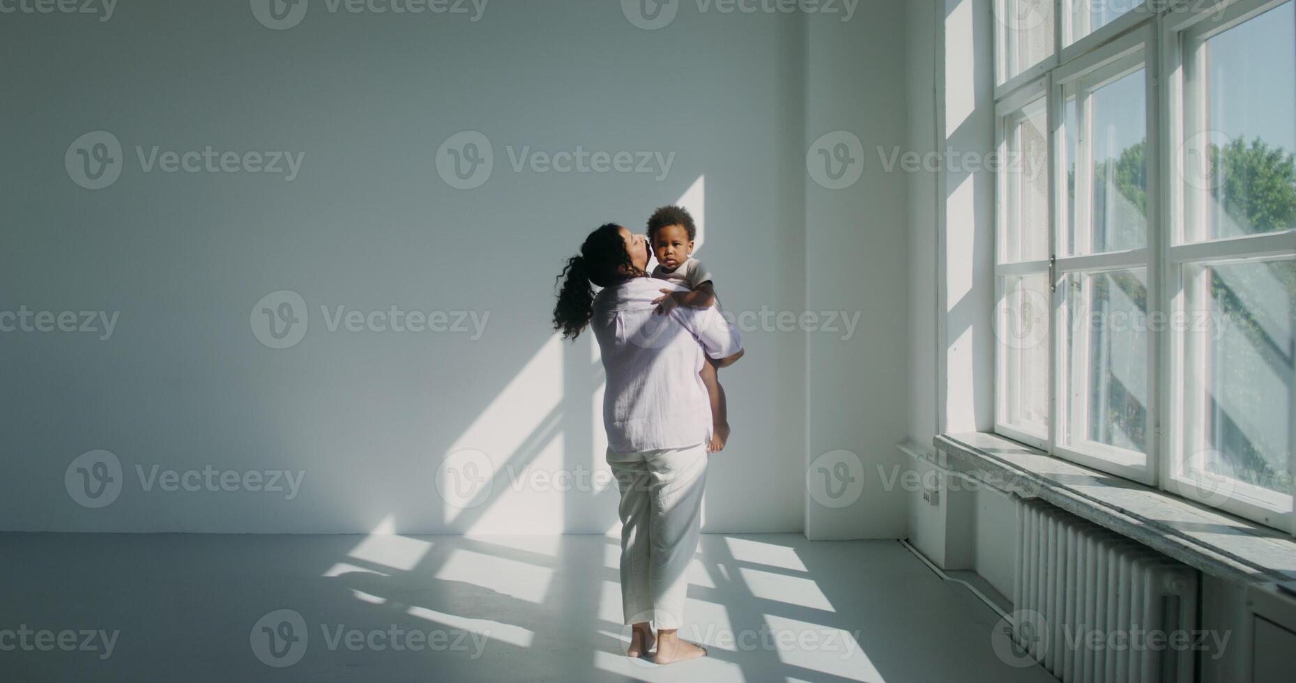 An African-American woman dressed in pastel-colored clothes holds her little daughter kisses her photo