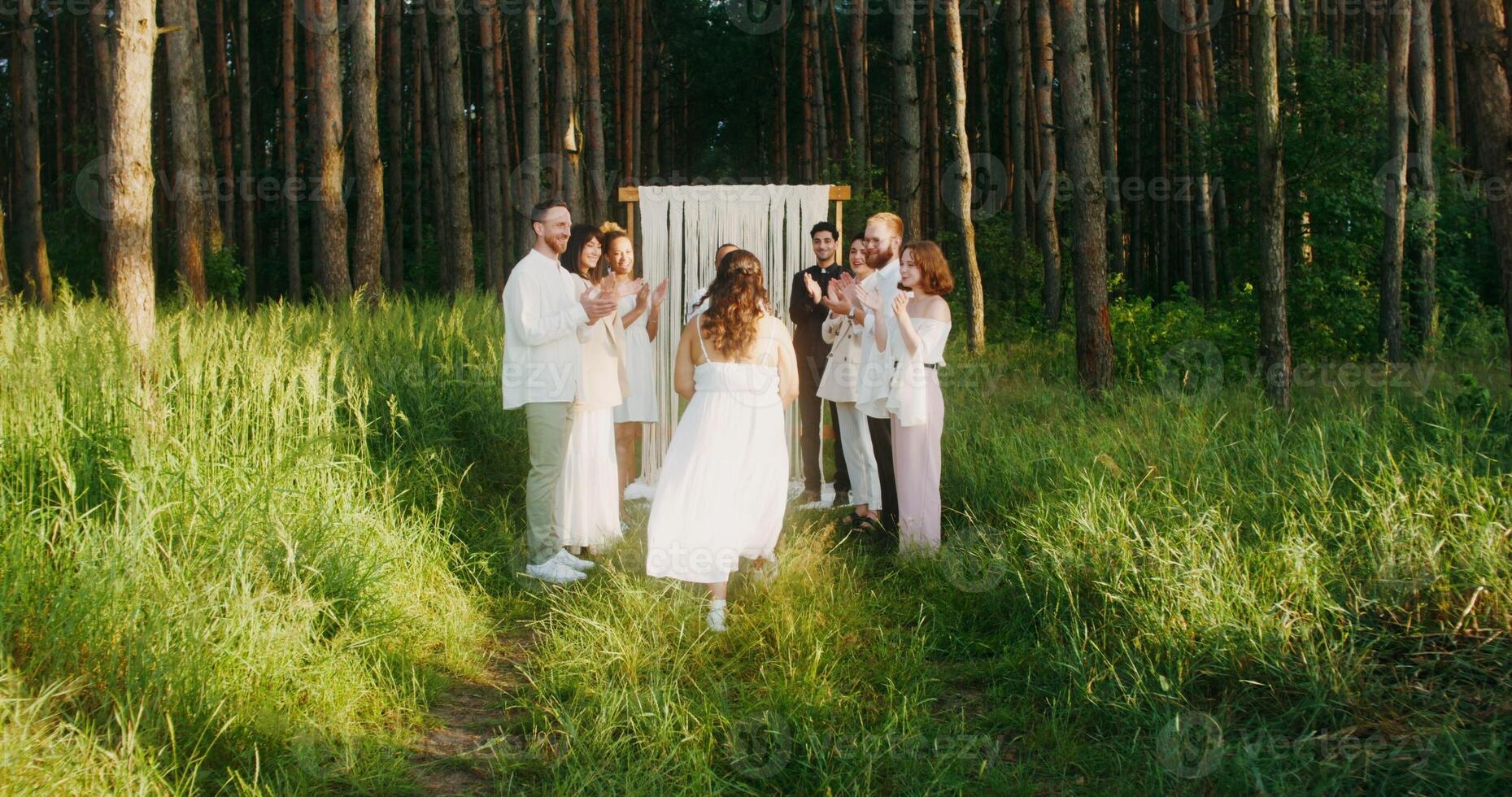 The bride goes to the groom past the applauding guests. Outdoor wedding with a priest - wedding photo