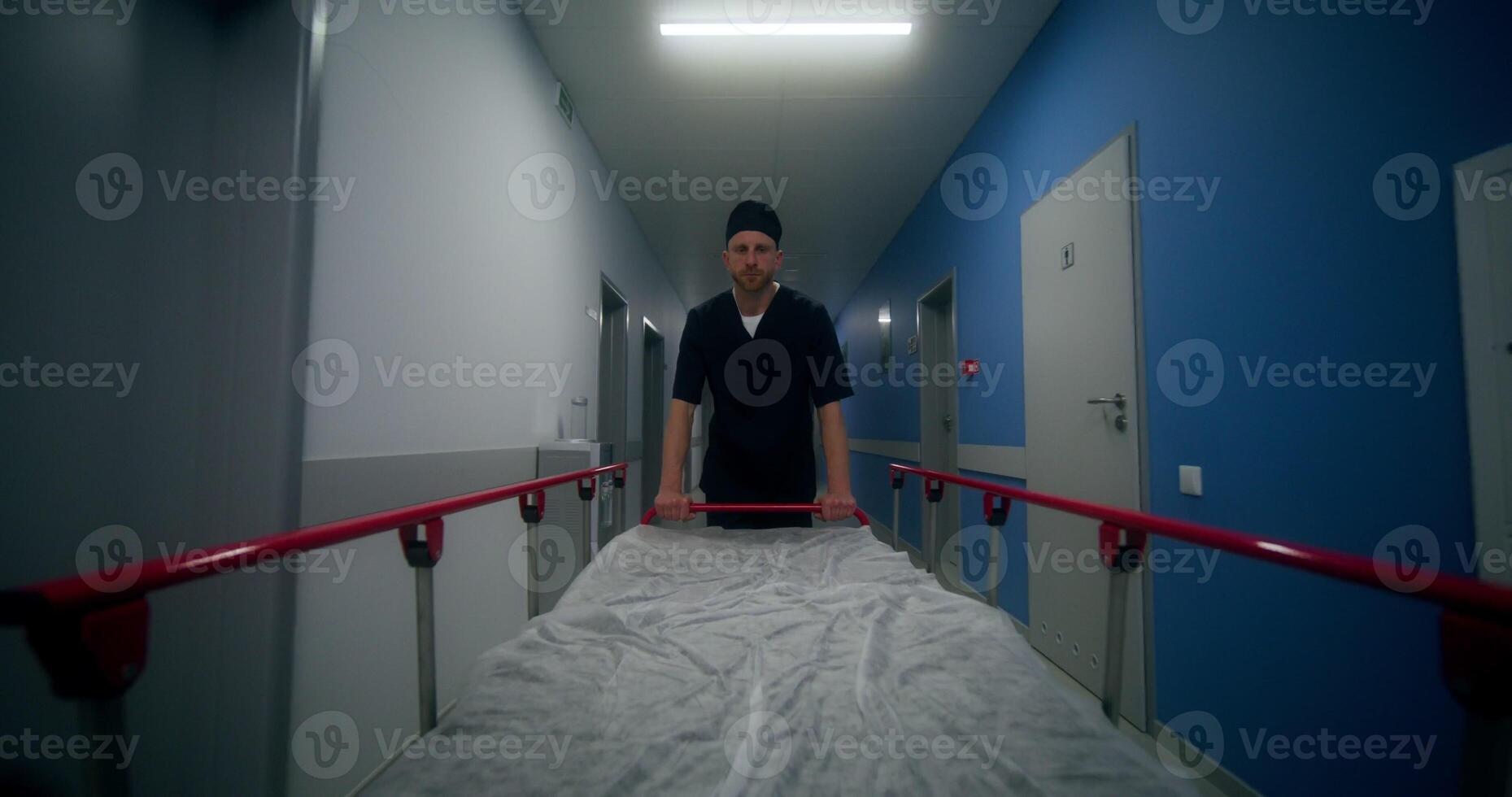 An orderly carries an empty gurney down the hospital photo