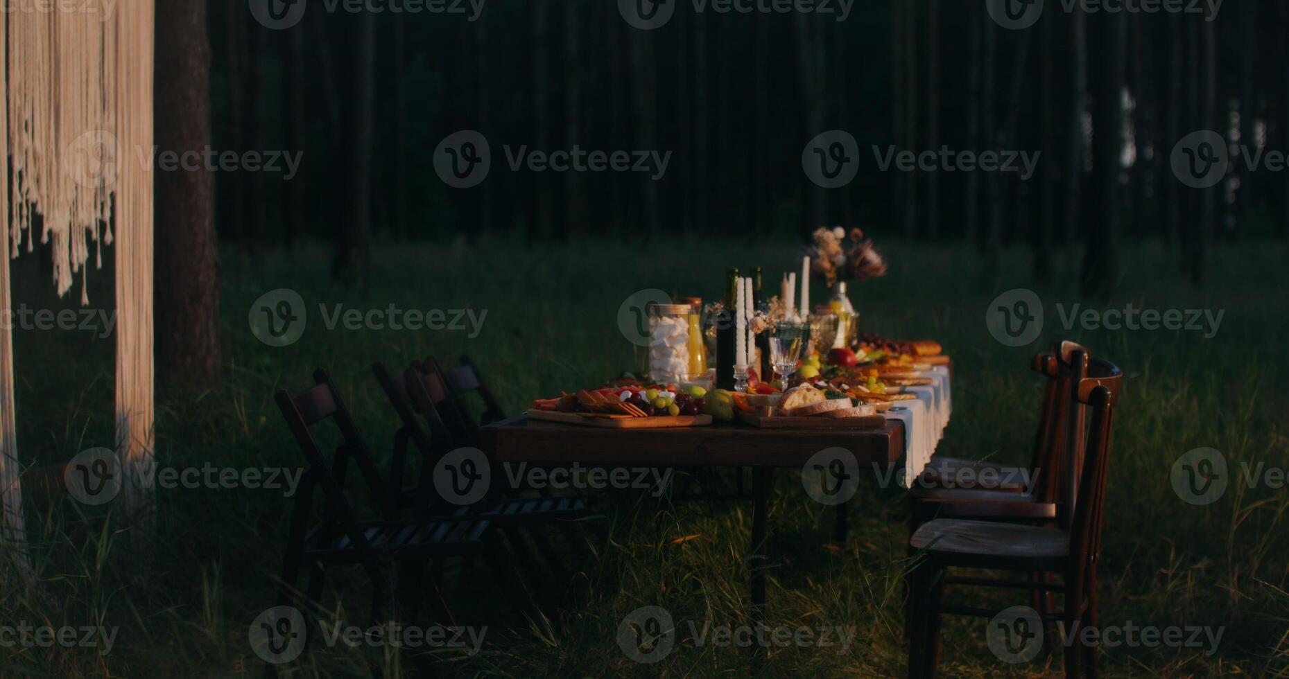 A beautiful festive table covered with a variety of food stands near a decorated arch in the forest at night photo