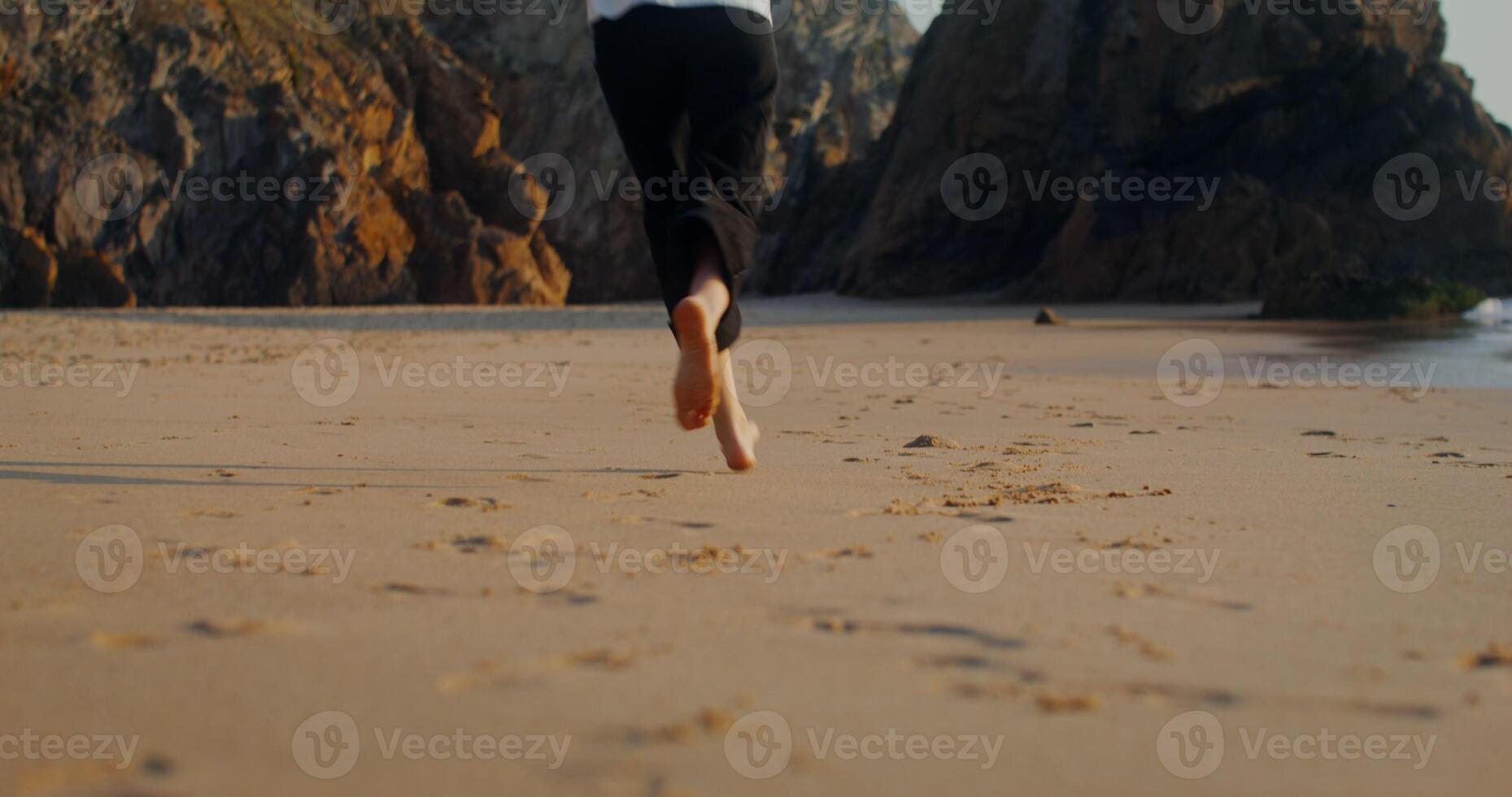 A young woman in casual clothes runs and spins along the seashore at the foot of a cliff photo