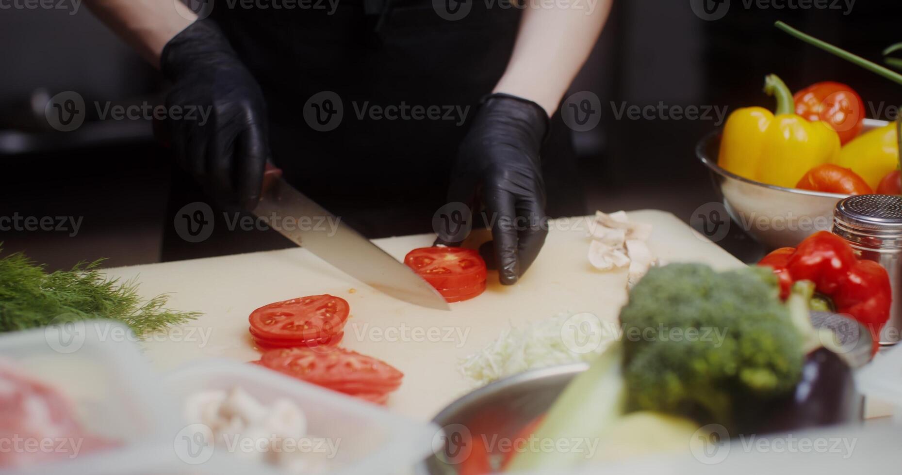 A woman in a chef's uniform with disposable black gloves on her hands cuts vegetables in the restaurant kitchen photo