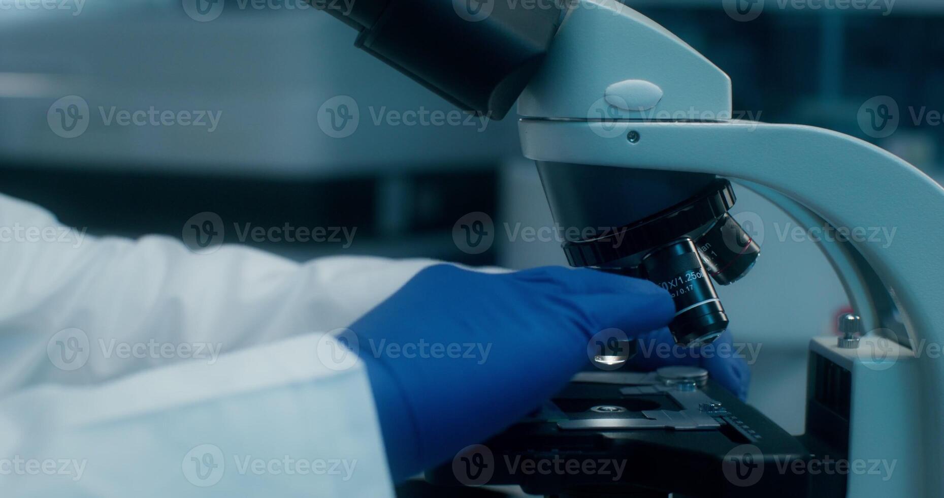 Man in a lab coat uses a microscope sitting at a desk in a medical laboratory. Close-up of his face photo