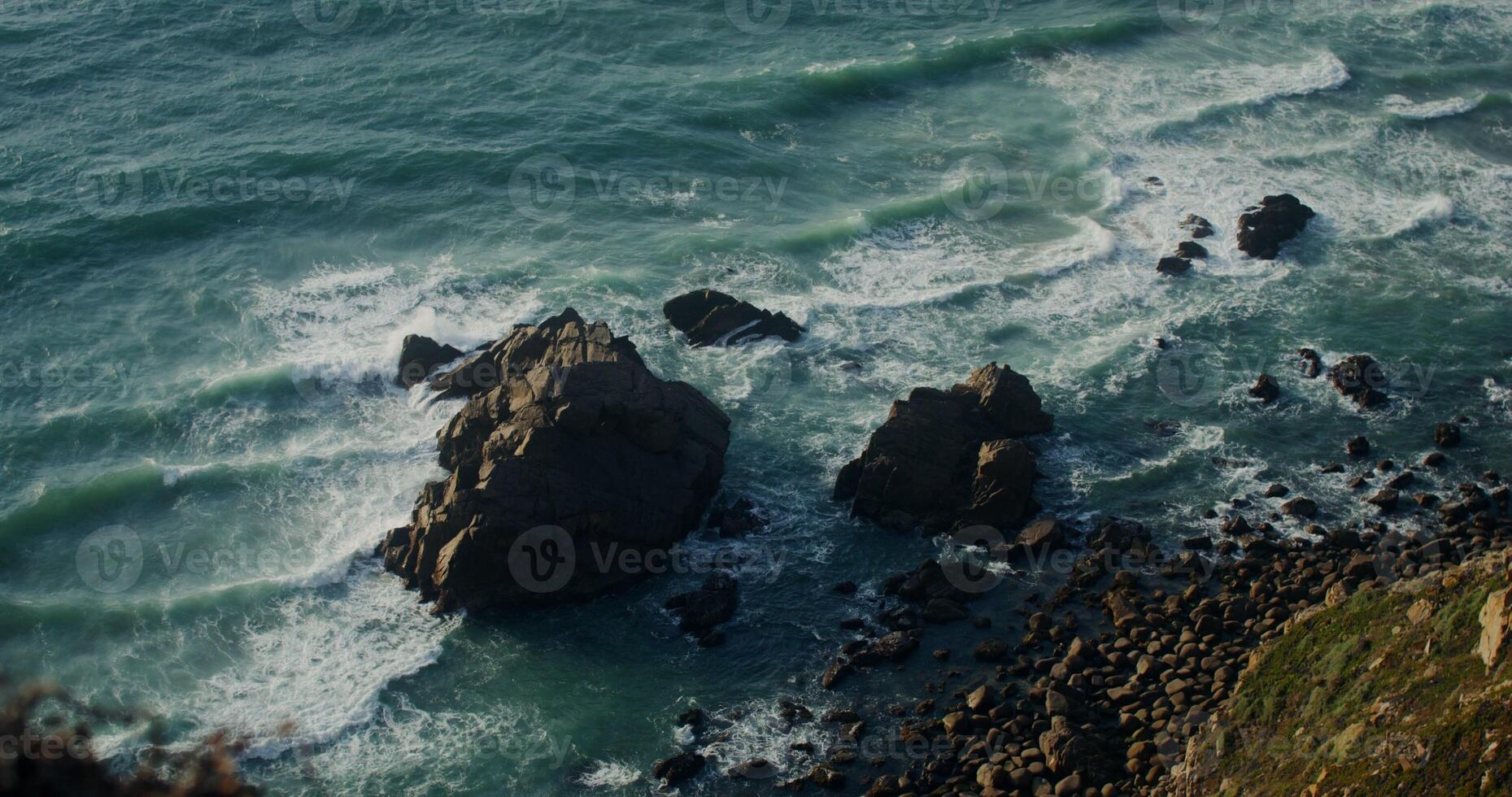 Top view of a rocky shoreline with sea waves crashing against the rocks. photo