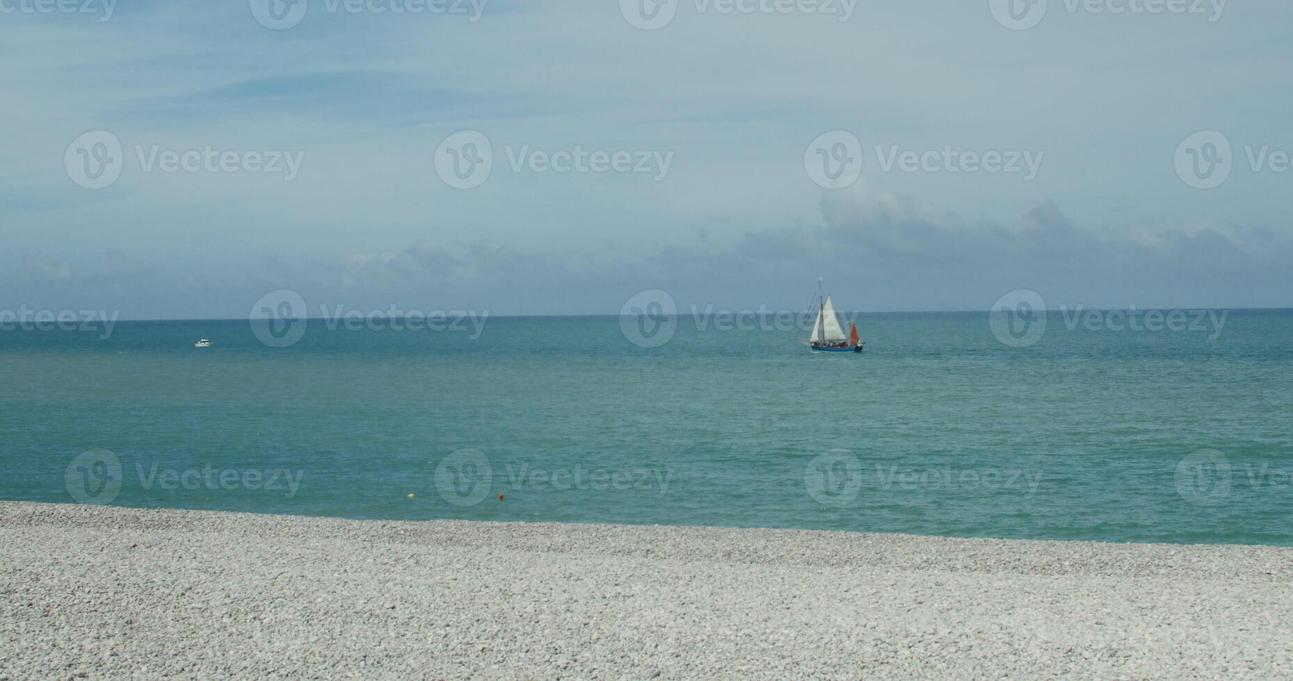 A sailboat floats on the sea near the pebble shore photo