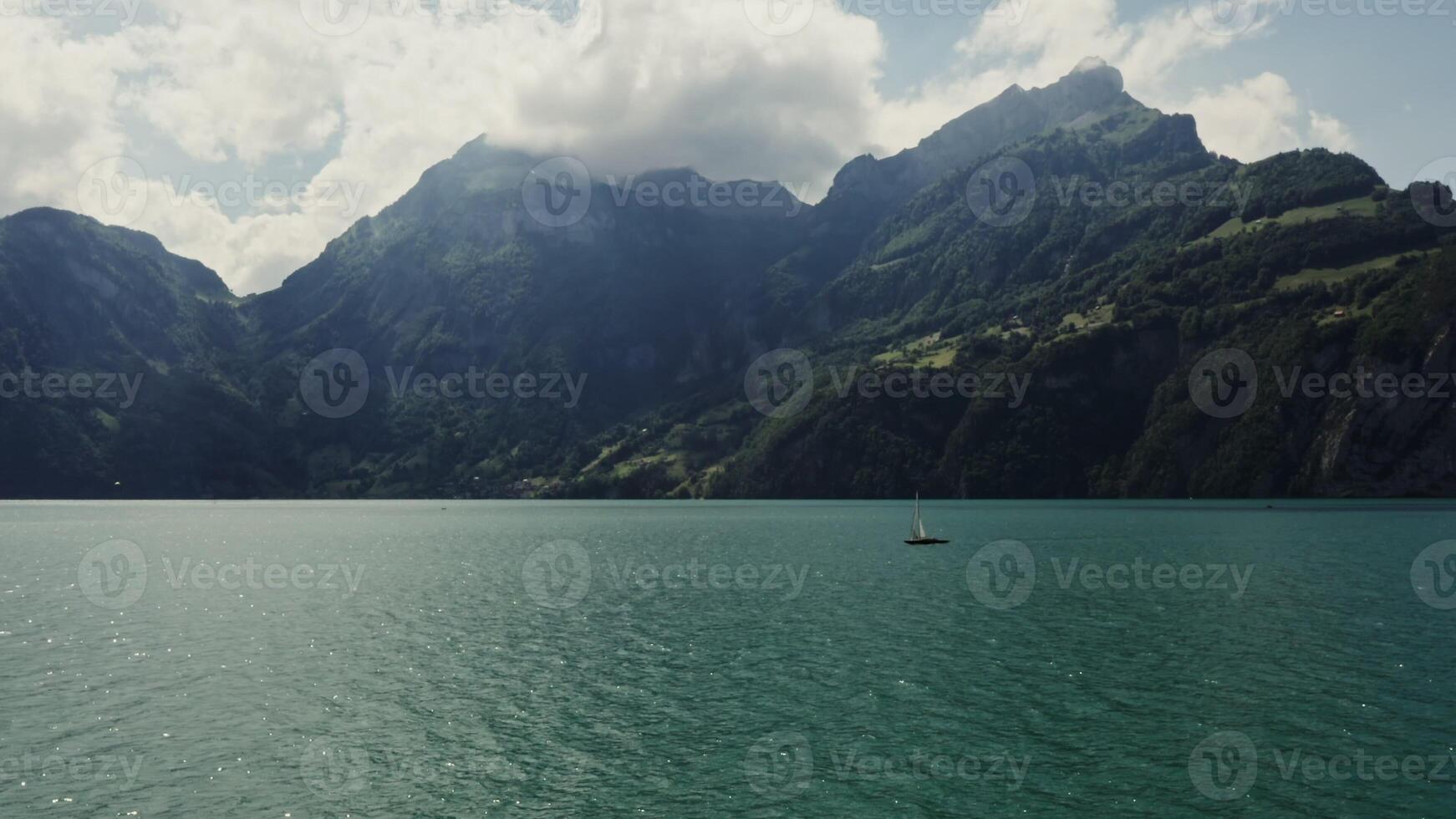 Sailboat floats on a picturesque lake at the foot of the Alpine mountains, the tops of which are covered with white clouds. Panoramic drone footage, Switzerland photo