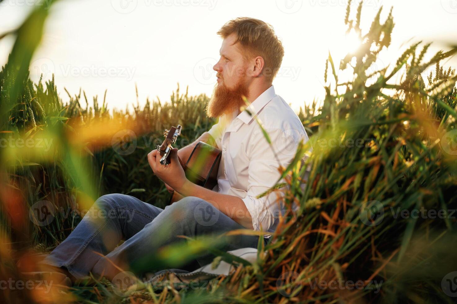 Country musician is with guitar ,on, the ,ground. Man in white shirt is on the agricultural field photo