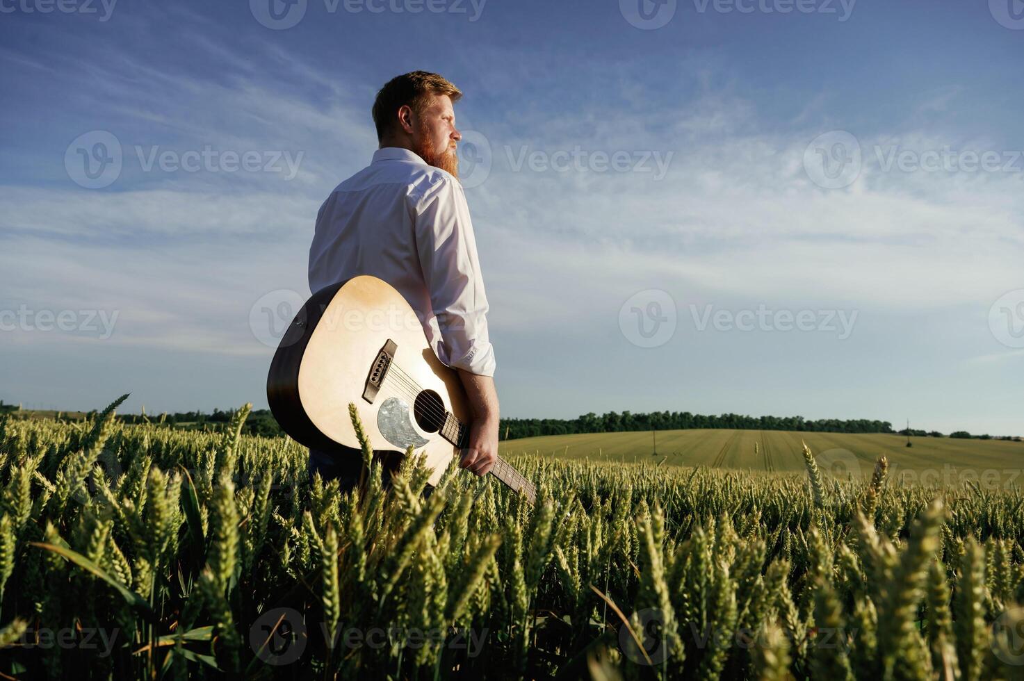 Musician is with acoustic guitar. Man, in ,white shirt is on the agricultural field photo