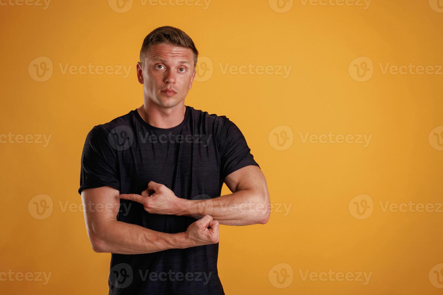 Biceps, pointing on it by finger. Man is against background in the studio photo