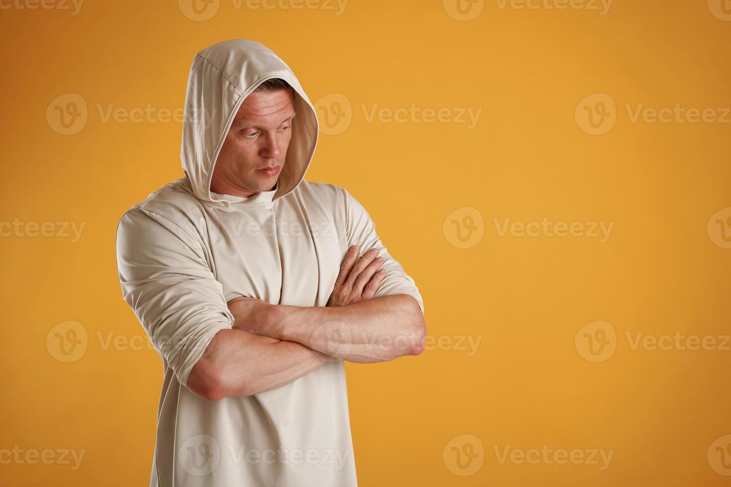 In the ,hoodie, with arms crossed, serious. Man is against background in the studio photo