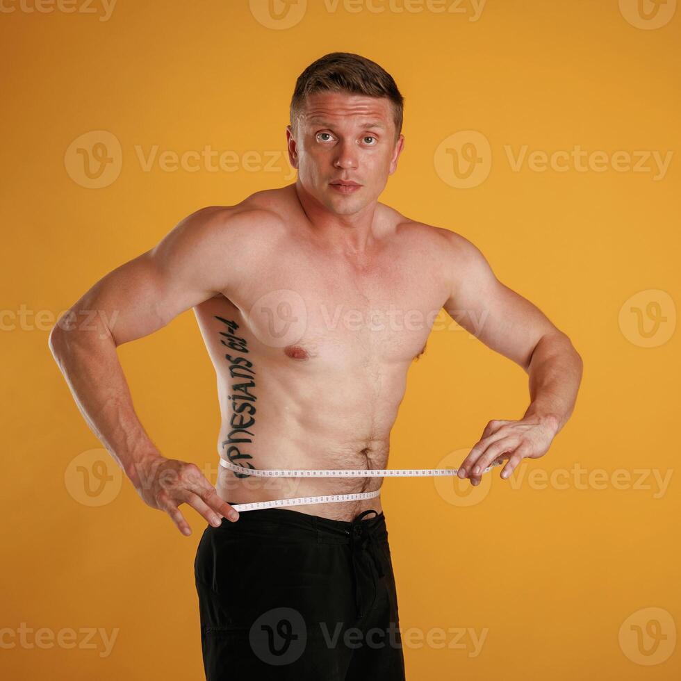Measuring ,the waist, muscular ,,guy. Man is against background in the studio photo