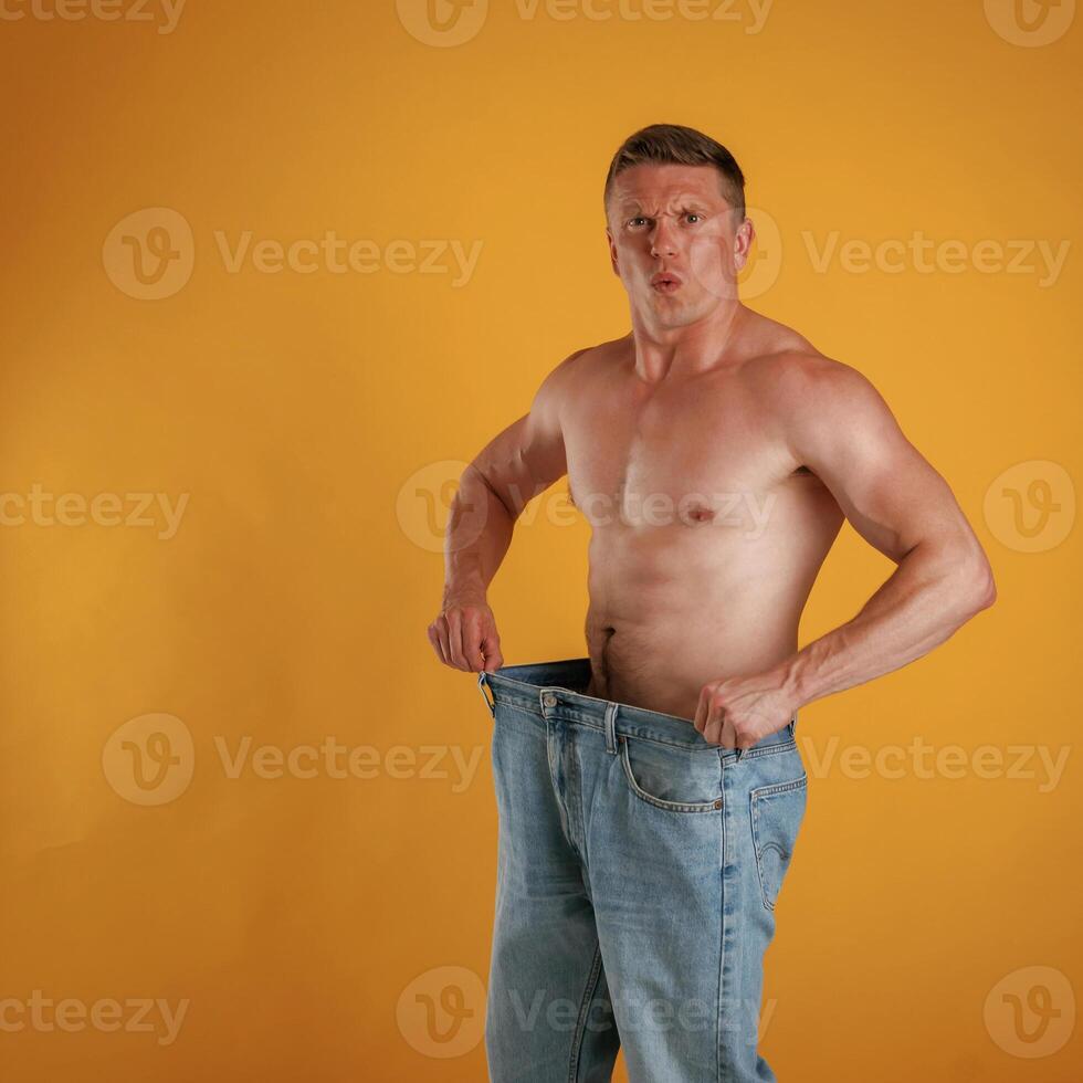 Weight,,, loss, shocked by results, big and huge pants or jeans. Man is against background in the studio photo