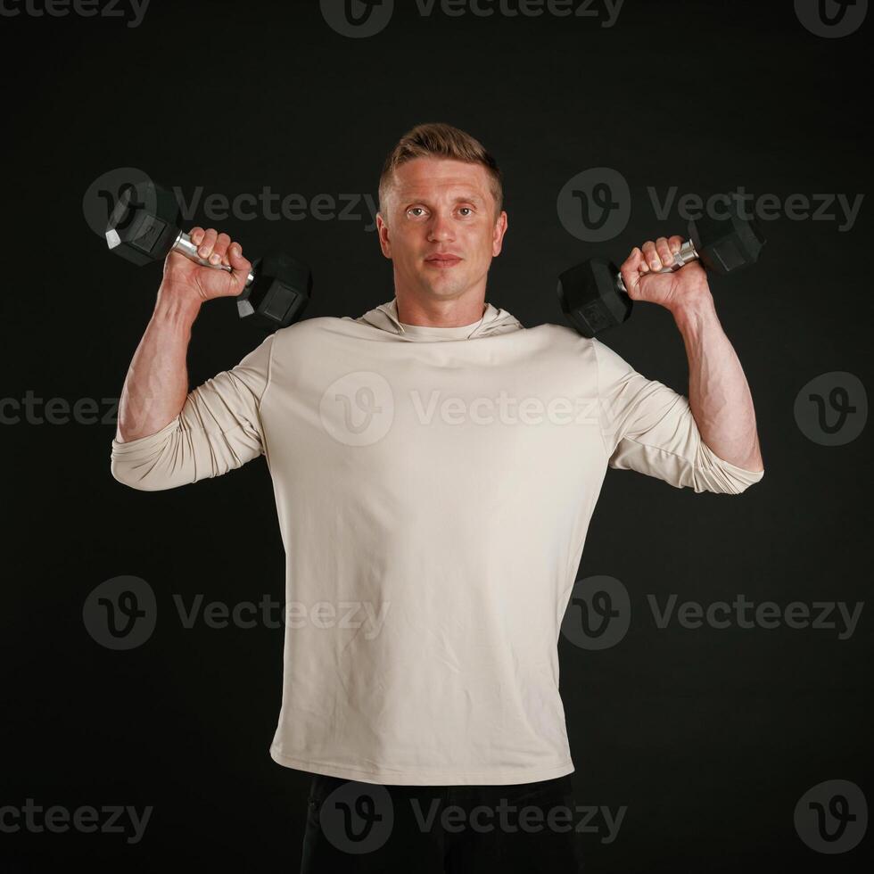 Powerful sportsman, is holding dumbbells. Against background in the studio photo