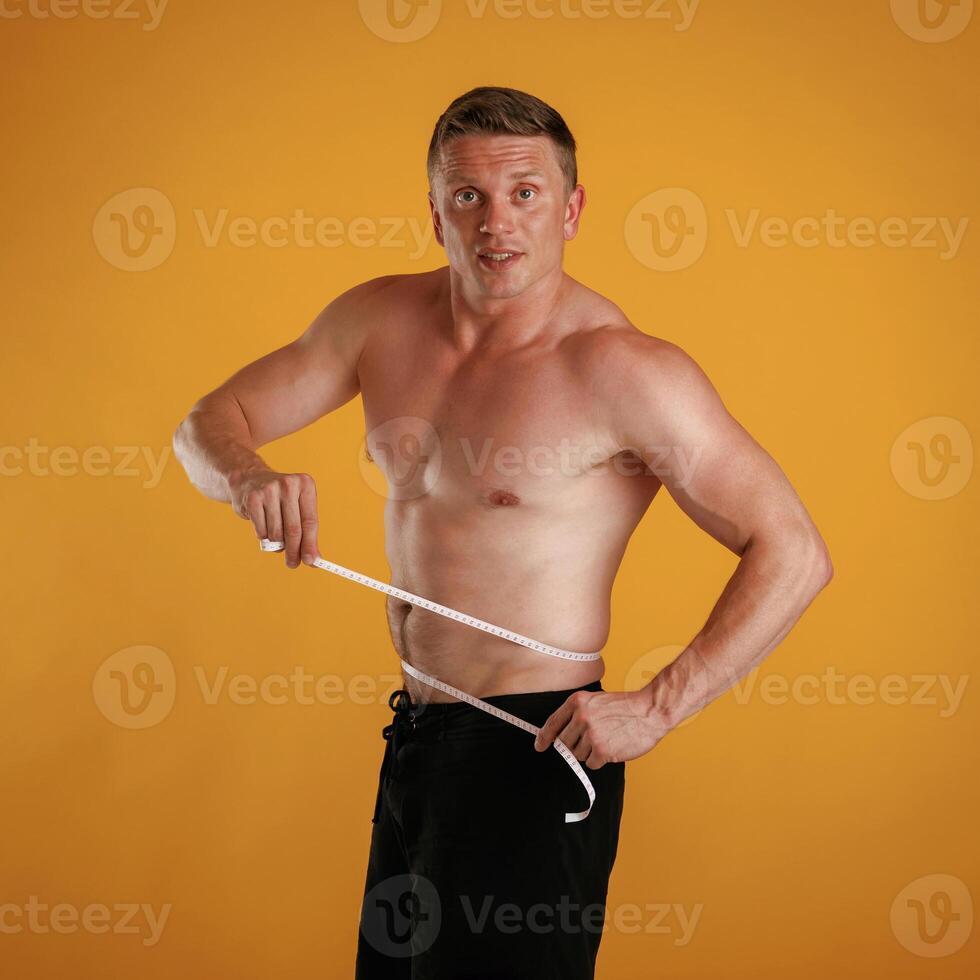 Measuring ,the waist, muscular ,guy. Man is against background in the studio photo