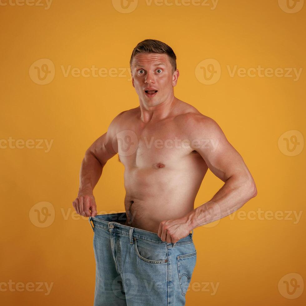 Weight loss,,, shocked by results, big and huge pants or jeans. Man is against background in the studio photo