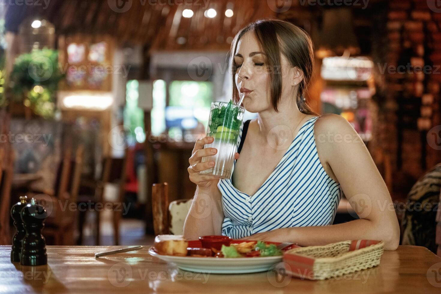 Drinking the mojito. .Woman is in the restaurant with food and drink photo