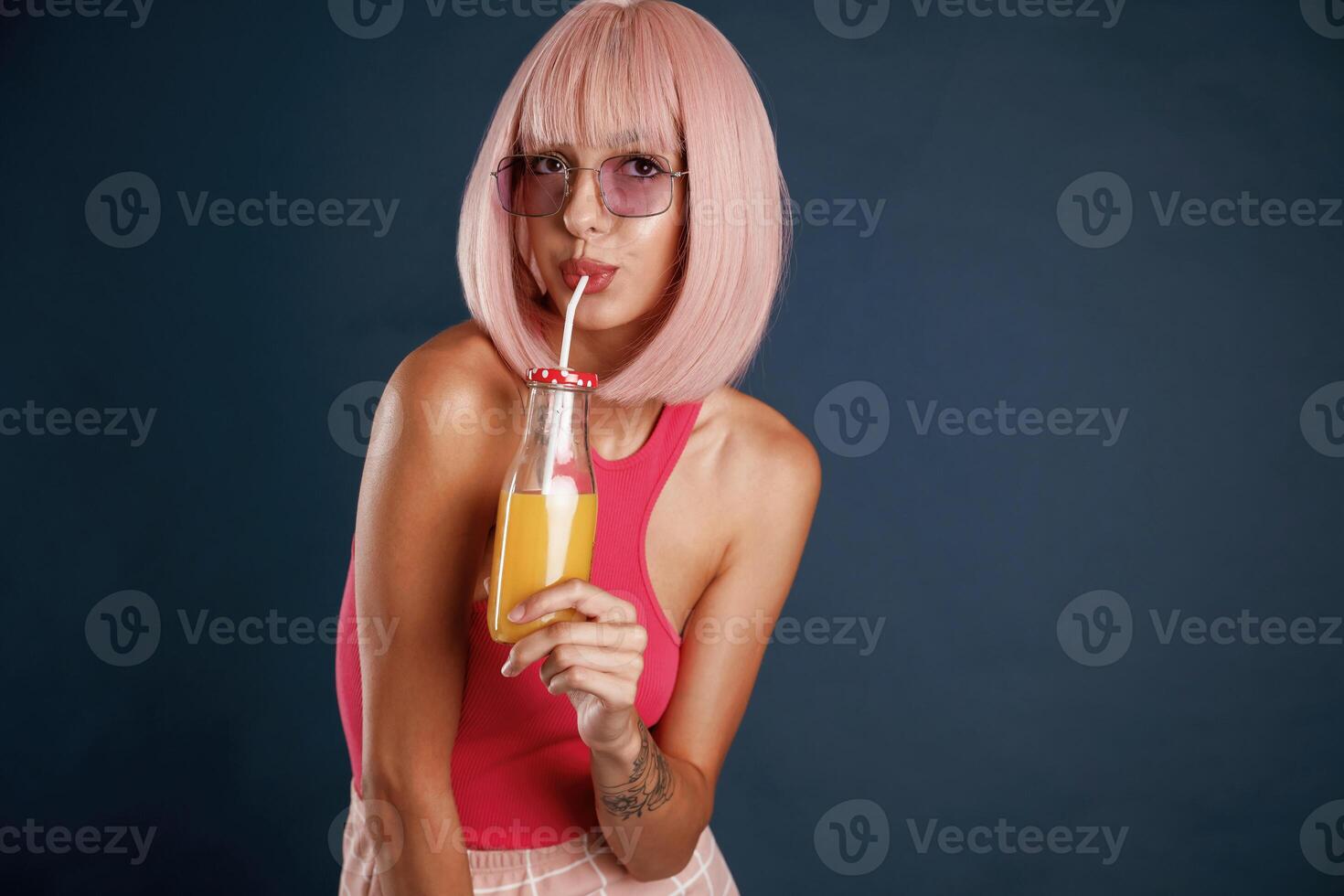 Pink hair, with orange juice. Beautiful young woman is against background photo