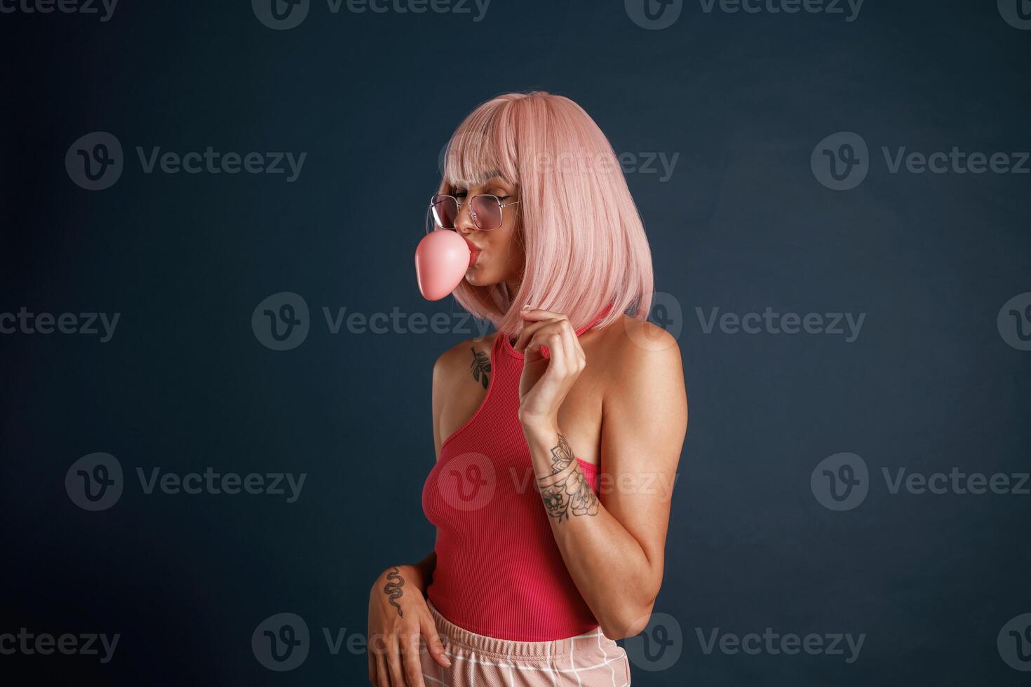 Blowing a gum bubble, pink hair. Beautiful young woman is against background photo