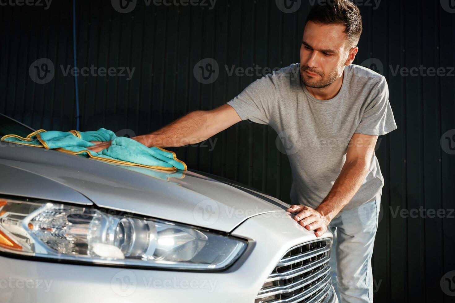 Guy, is ,polishing,, the surface of automobile by using cloth. Man is with his car outdoors photo