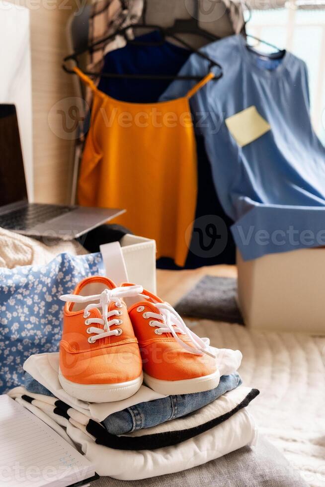 Bright orange shoes neatly placed on folded minimalist clothes with background of color-coded tops on hangers showing decluttering and capsule wardrobe organization in progress with checklist notes photo