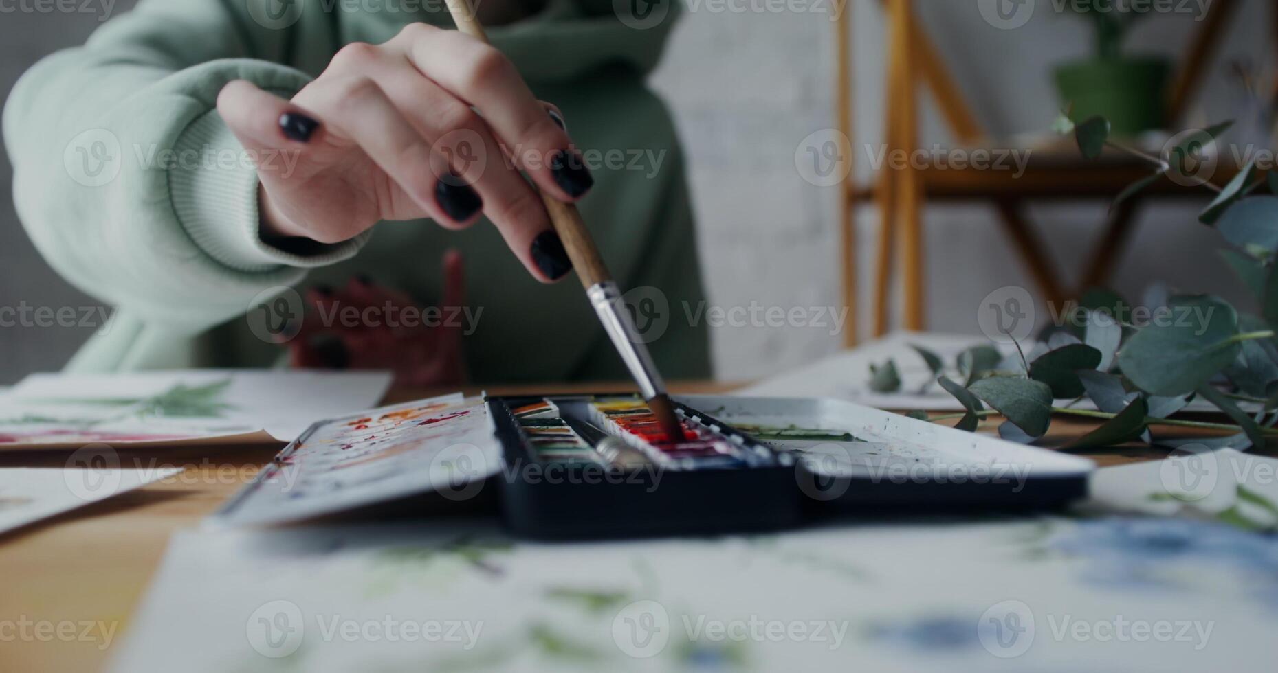 Female artist mixes watercolors with a brush to get the right color while painting wild flowers on paper. Close-up of female hands with brush photo