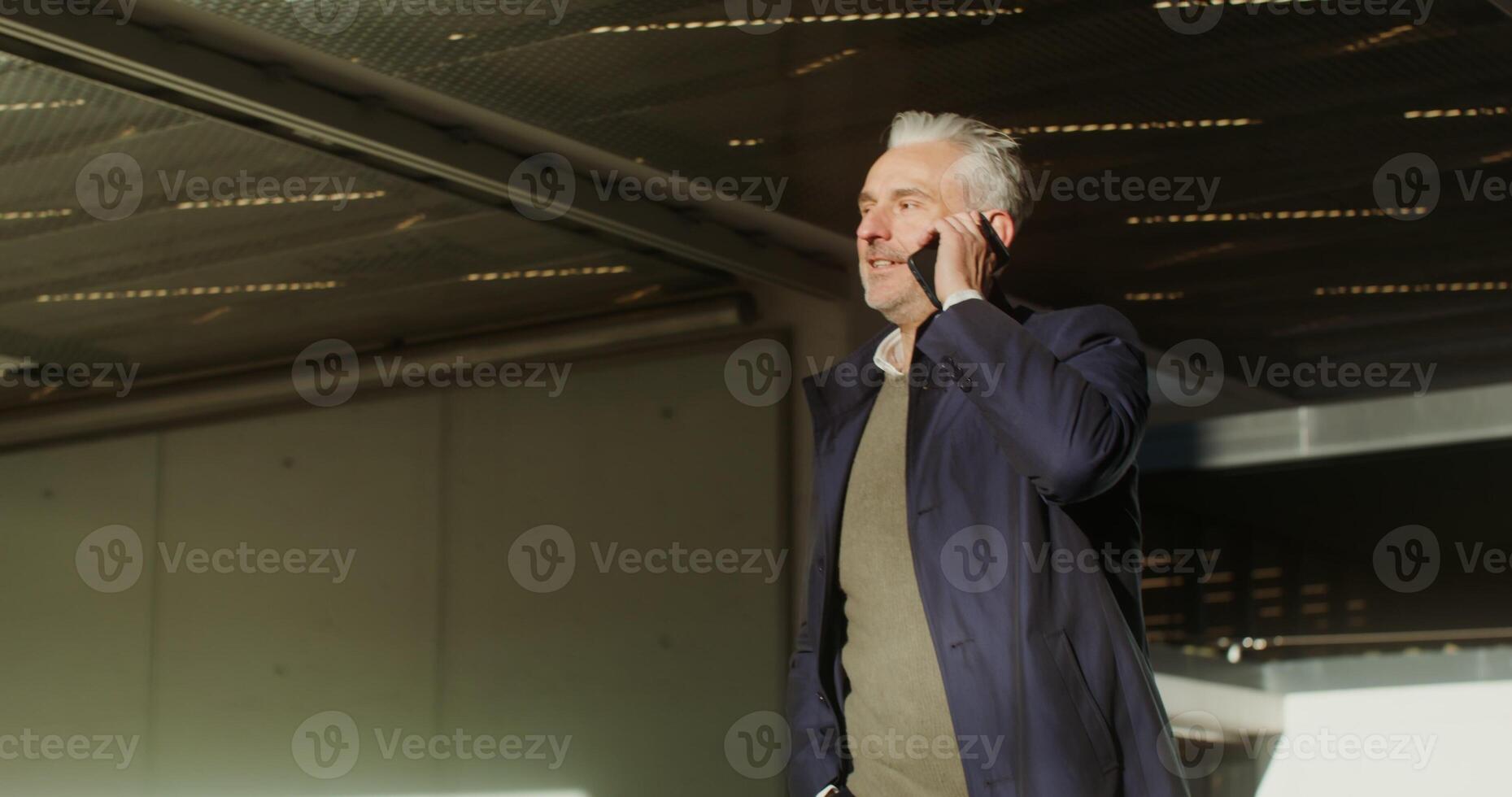 A respectable gray-haired man of European appearance, dressed in a coat, is talking on a mobile phone photo