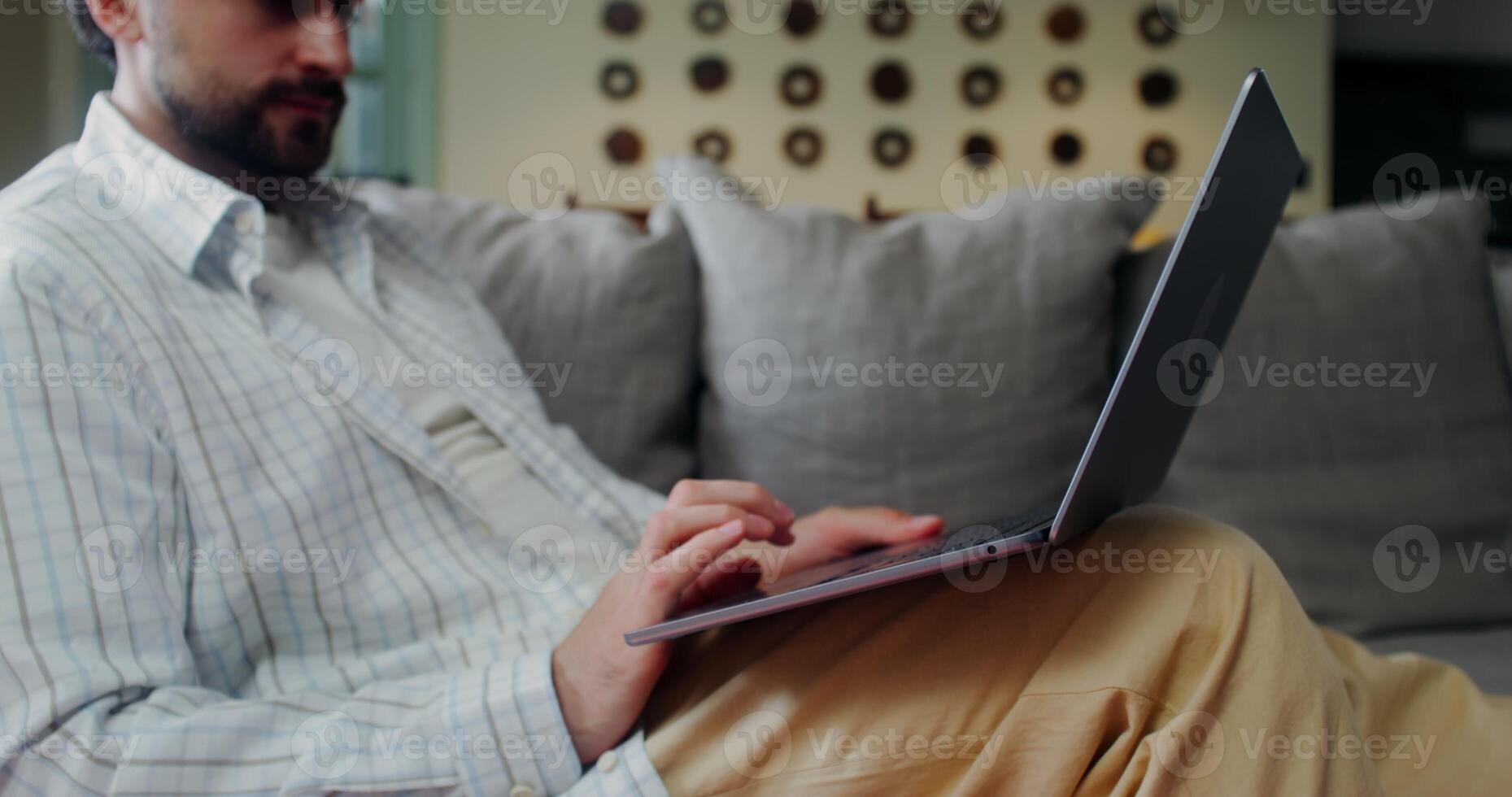 Stylish man in casual clothes starts a call on a laptop smiling and waving hello while sitting on a sofa at home photo
