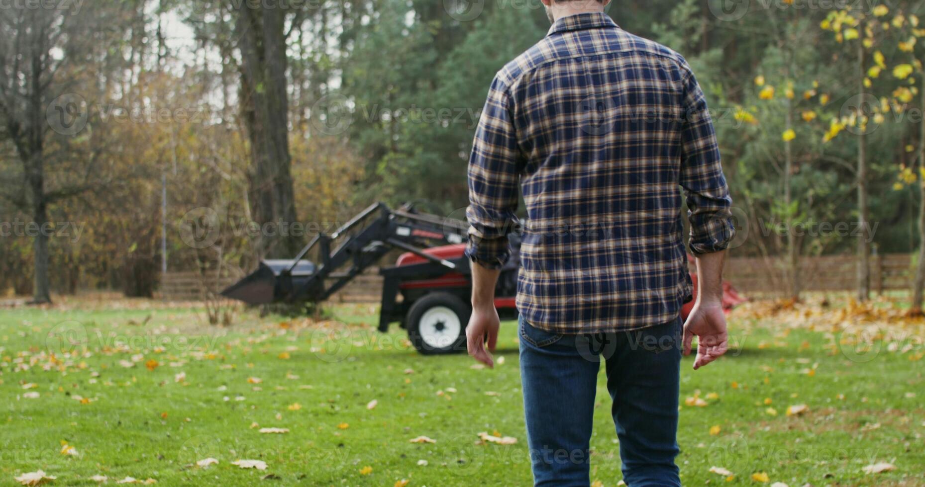 Black-haired man with a beard, dressed in casual clothes with a baseball cap on his head, walks up to the tractor and gets into it, getting ready to work in the field photo