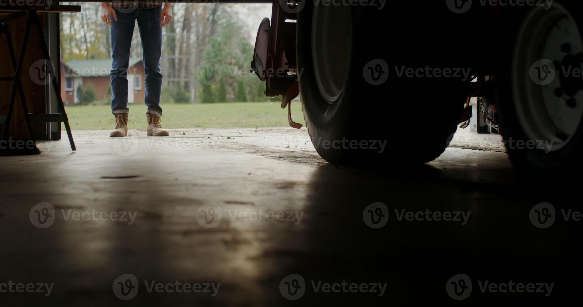 Man walks into an indoor garage approaching a tractor, male legs in stylish brown boots close-up photo