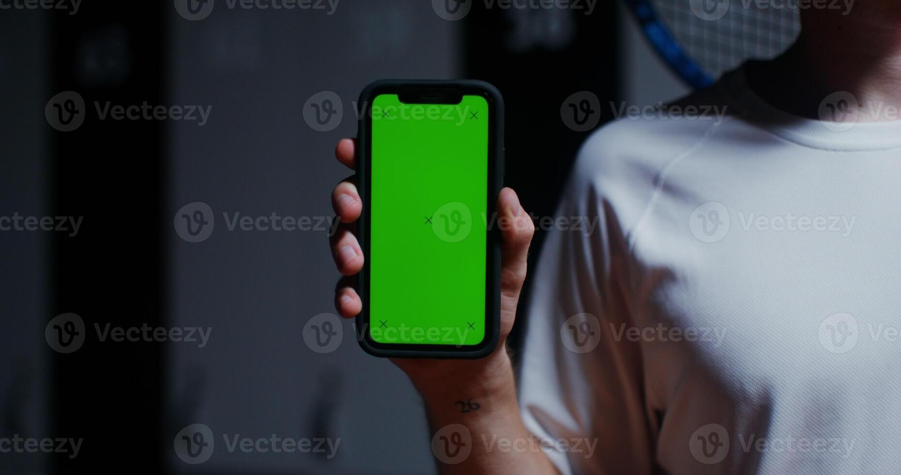 Young man with a racket in his hand holds a phone with a green screen, standing in the locker room of the sports hall. Close-up phone, man's face is not visible, copy space photo