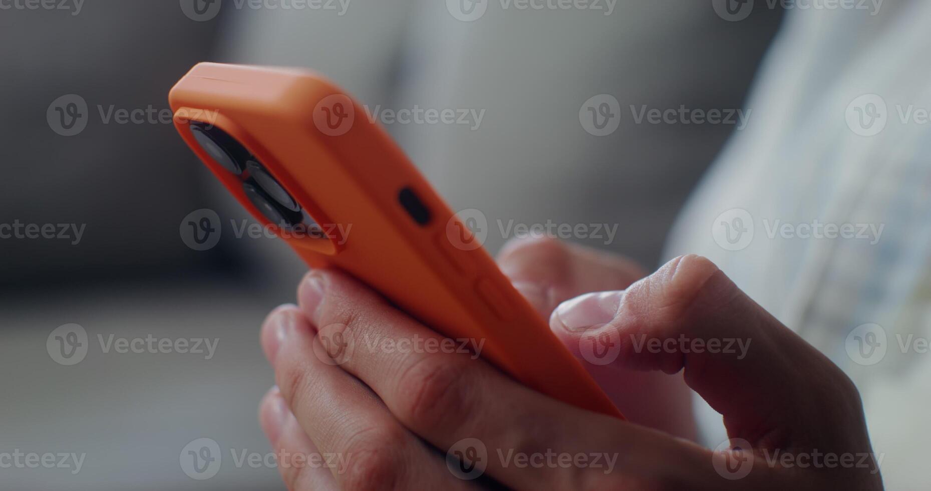 Close-up of a mobile phone in an orange case in men's hands. Man typing on smartphone, no face photo