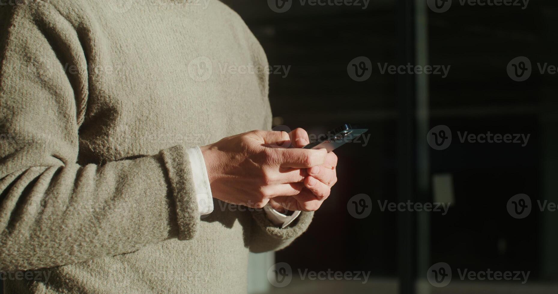 Man dressed in a warm sweater is typing a message on his phone using the Internet while walking around the city. Close-up of male hands, no face. in 4k, red komodo photo