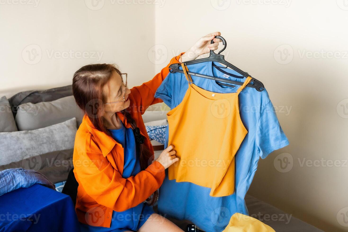 This moment captures a home-based digital side hustle. A woman documents her clothes for resale while embracing decluttering, minimalism, and sustainable fashion choices in a cozy domestic setting photo