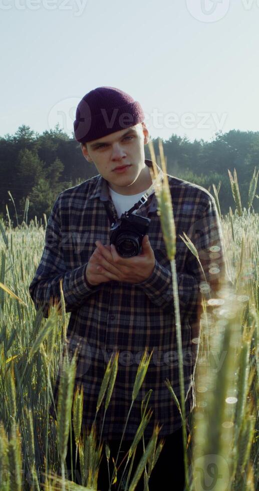 A man takes photos with a camera, standing between ears of wheat in an agricultural field on a summer sunny day. 4k vertical , red komodo