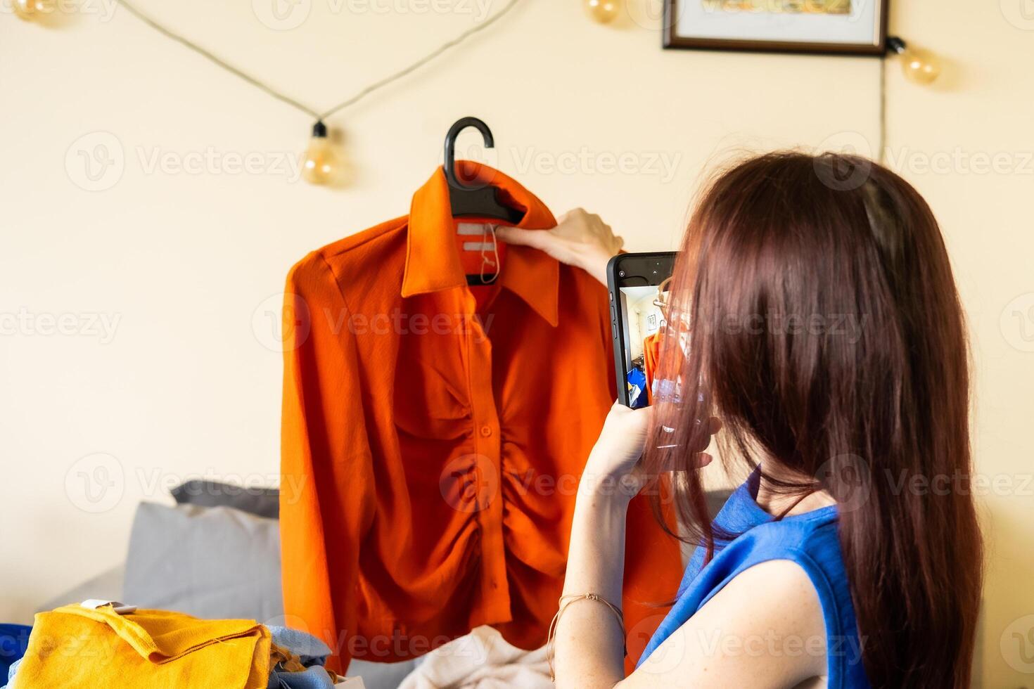 Woman uses her smartphone to take product photos for resale from home combining digital side hustle with mobile content creation and sustainable fashion practices in modern lifestyle economy