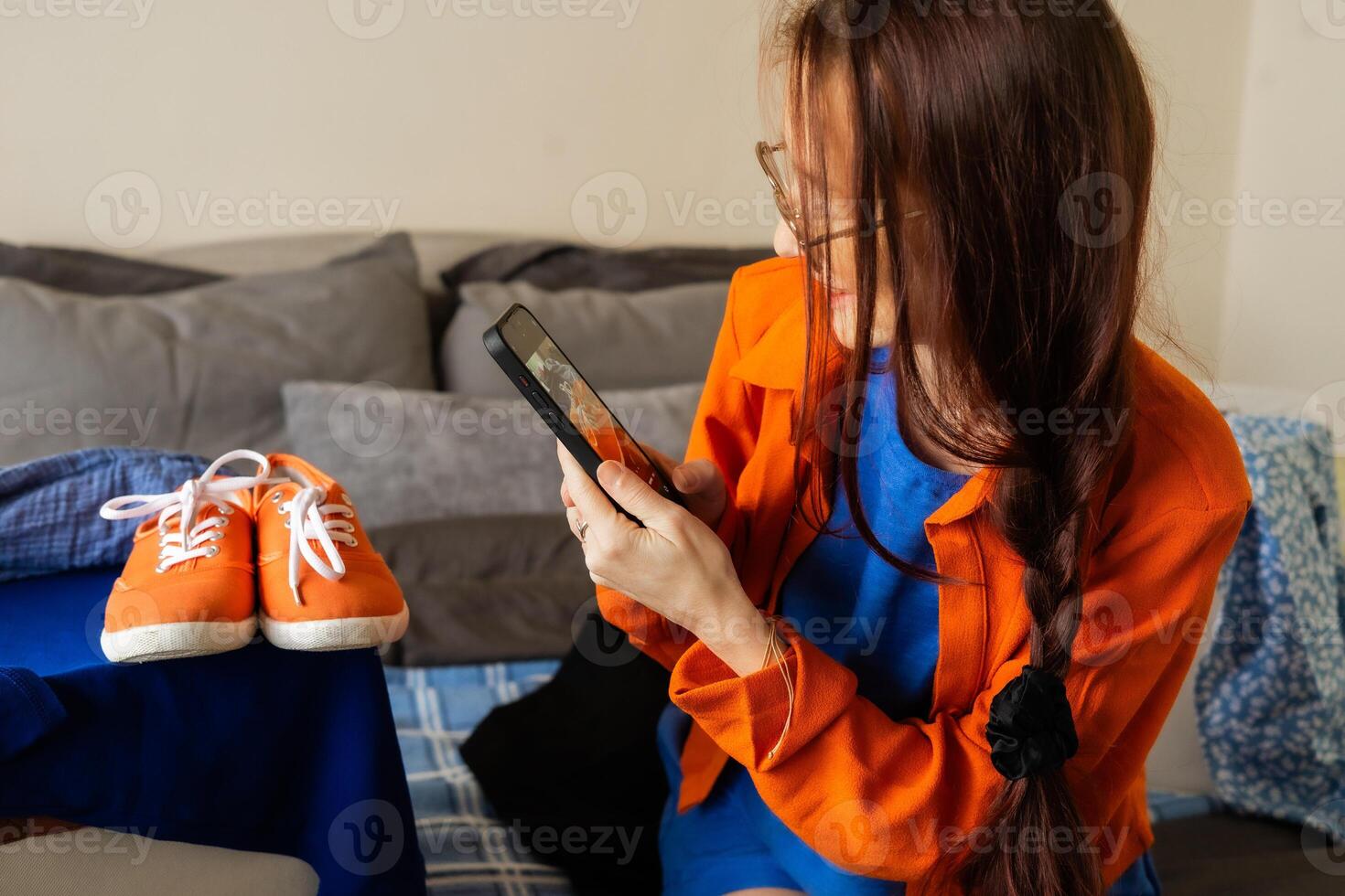 Woman takes photo of orange sneakers for online resale while embracing sustainable fashion values, decluttering her space, and telling a story of mindful consumption through everyday digital content