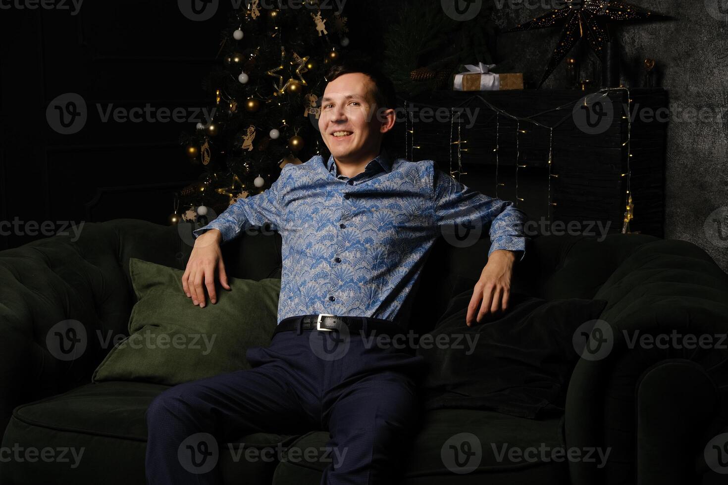 A Happy Man is Relaxing on a Comfortable Couch Surrounded by a Beautiful Christmas Tree photo