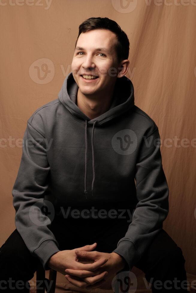 A Cheerful Young Man Wearing a Casual Hoodie is Sitting and Posing for a Portrait photo
