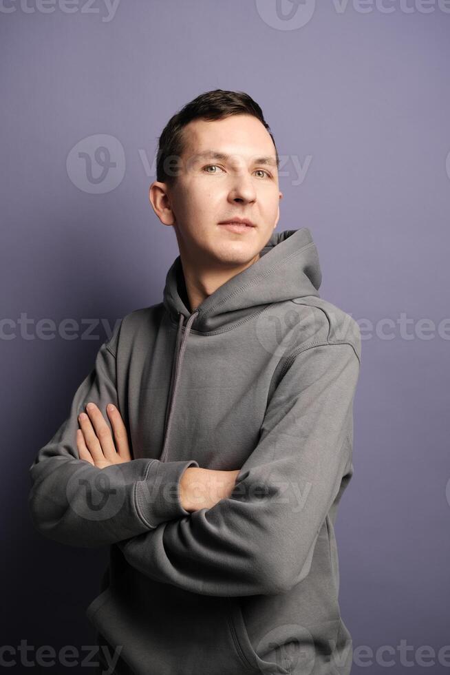 A Confident Man Dressed in a Gray Hoodie Posing Against a Vibrant Purple Background photo