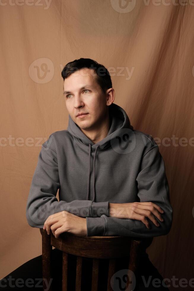 A Reflective Young Man, Dressed in Casual Attire, is Sitting Comfortably and Relaxed on a Chair photo