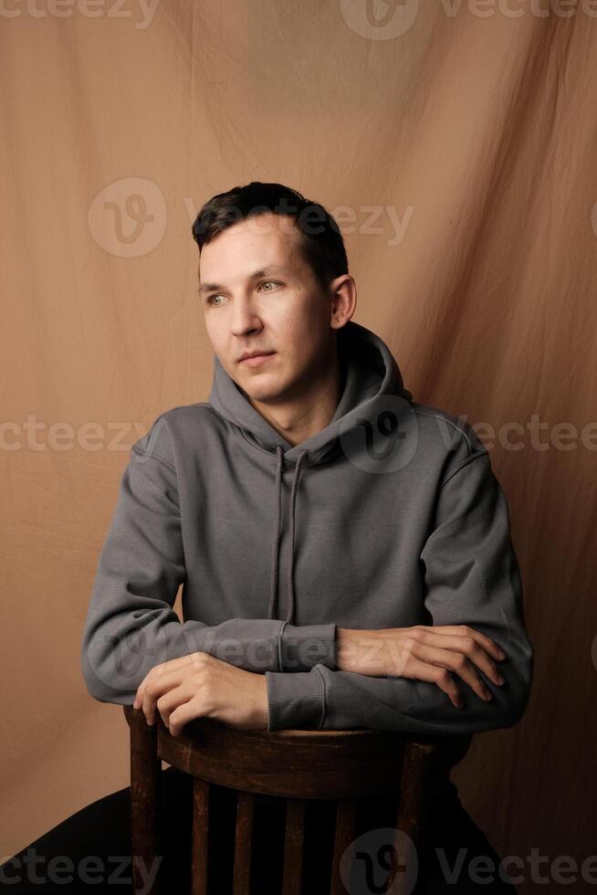 A Contemplative Young Man Dressed in a Casual Hoodie Sitting Comfortably on a Chair photo