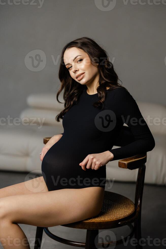 Pregnant model sitting on chair and touching belly photo