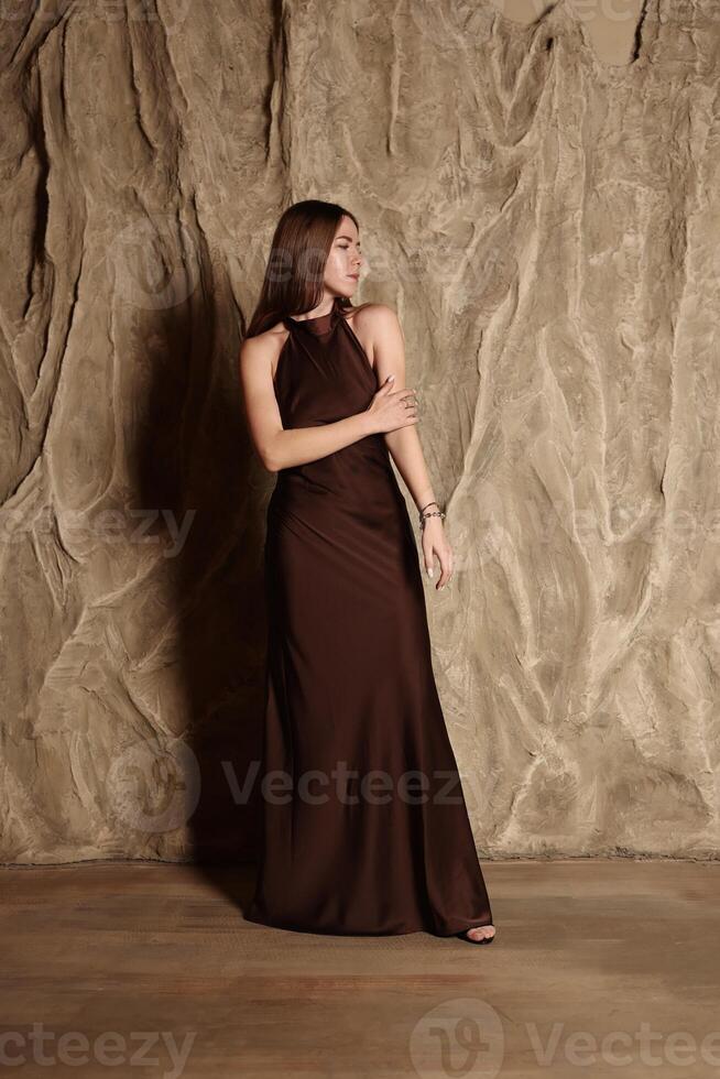 An Elegant Model Dressed in a Beautiful Brown Dress Posing Gracefully Against a Textured Background photo