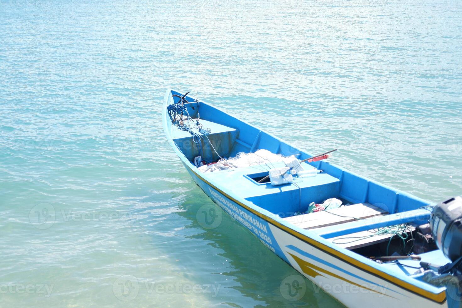 A blue fishing boat floating on the ocean under a bright sunny day photo