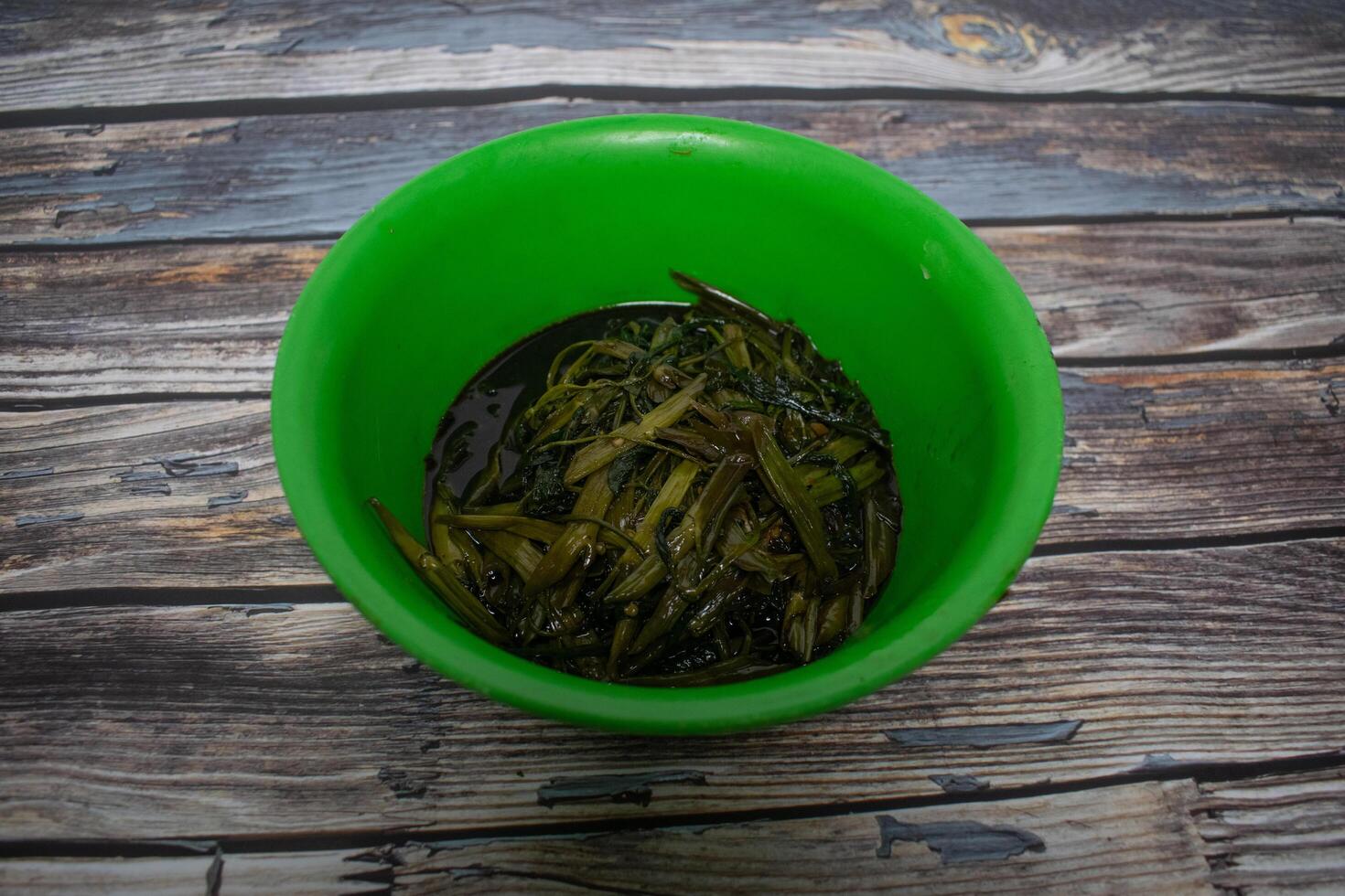 A bowl of cooked water spinach soaked in dark soy sauce, served in a bright green plastic bowl. photo