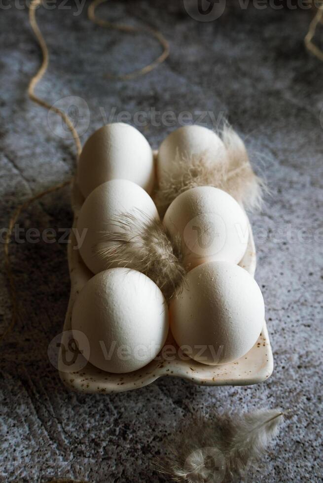 6 chicken eggs standing with feathers in a ceramic stand on a gray background photo