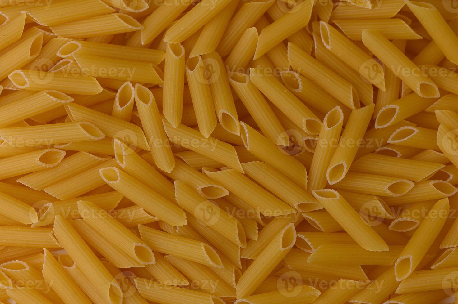 Uncooked mezze penne rigate pasta spread as a warm-toned food background. High-resolution texture. photo