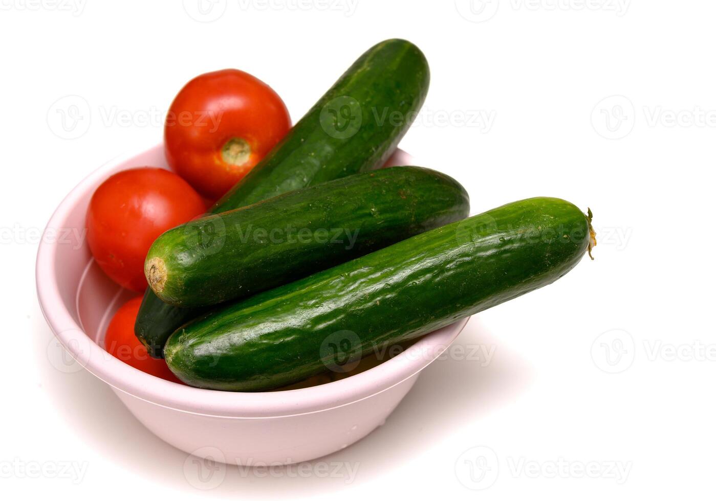 Bright red tomatoes and crisp cucumbers in a ceramic bowl on a table, prepared for a healthy fresh salad. photo